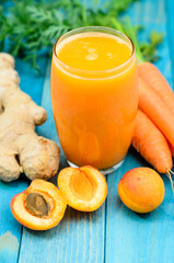 Glass of apricot and carrot juice on colourful turquoise blue painted wooden boards