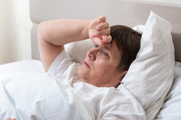 Fototapeta na wymiar Sick elderly woman on the bed. Grandma has a bad headache.