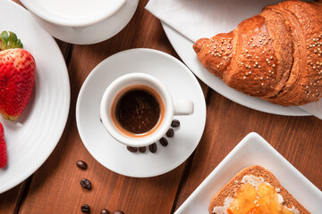 Tazzina di caffè espresso in tavola accompagnata da cornetto, latte, fette biscottate e frutta fresca 