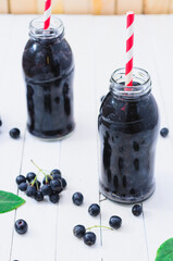 Cold delicious juice made of chokeberries on white wooden boards. Top View