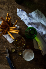 Glass of light beer on a dark brown table with snacks. Top View