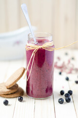 Cranberry and black currant smoothie in glass jars with cookies on a white wooden background