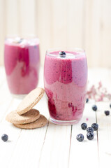 Cranberry and black currant smoothie in glass with cookies on a white wooden background