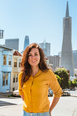 Cute young woman walks along a beautiful street with a view of the Transamerica Tower in San Francisco