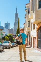 A young man walks along a beautiful street with a view of the Transamerica Tower in San Francisco