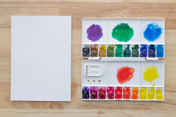 Watercolor paints set in white palette with white paper background.