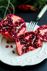 Pomegranate sitting on a retro plate. Moody, dramatic light shining in from the right. Pomegranate seeds are spilling out onto the table  Christmas Eve Table Decoration