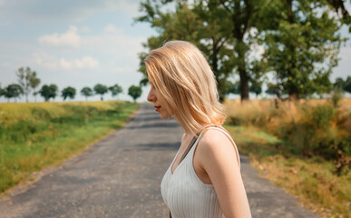 Fototapeta na wymiar Woman with blond hair and white clothes stay on country road