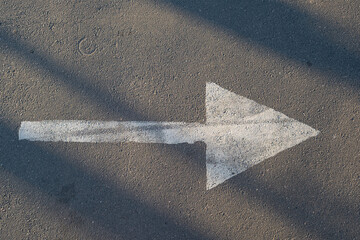White drawn arrow indicating the direction on an asphalt road. Copy space. Top view.