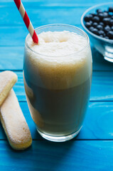 Glass of ice Coffee with cookies and bowl of chockberries on colourful turquoise blue painted wooden boards
