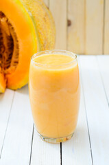Glass of fresh organic cantaloupe melon smoothie on white wooden boards.