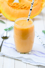 Glass of fresh cantaloupe smoothie with straw birch  on white wooden boards.