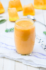 Glass of fresh cantaloupe smoothie with straw birch  on white wooden boards.