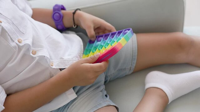Portrait blonde boy with pop it sensory toy different forms. Boy presses colorful rainbow squishy soft silicone bubbles in children's playroom. Stress and anxiety relief. Trendy fidgeting game.