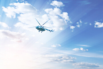 A helicopter flies high in the blue sky, in the rays of the sun and clouds. Rescue operation....