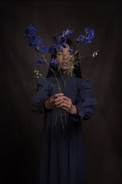Studio art portrait of girl holding bouquet of blue flowers