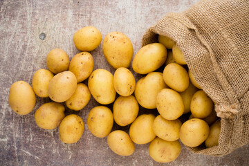 Sack of fresh raw potatoes on wooden background, top view.