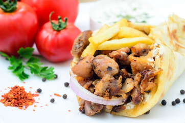 Plate of traditional Greek pita gyros with meat, fried potatoes, tomato and onion