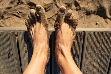 Women feet with sticky wet sand stand on the pier, on the beach, on a sunny summer day. Top view. 