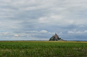 mont saint michel on a cloudy day with cornfield in the foreground 