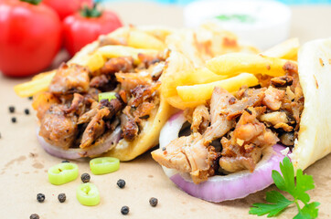 Traditiona Greek pita gyros with meat, fried potatoes, tomato, onion and drink on brown Paper, Placed on blue Wooden Table