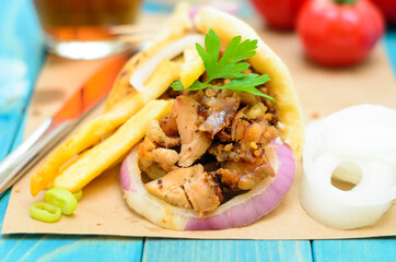 Traditiona Greek pita gyros with meat, fried potatoes, tomato, onion and drink on brown Paper, Placed on blue Wooden Table