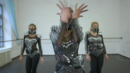 Medium shot confident dancers in costumes with respirator walking in slow motion looking at camera moving hands. Artistic talented Caucasian young women rehearsing indoors. Live camera