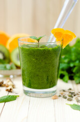 Healthy green smoothie with spinach, kiwi and orange in a glass on light wooden table