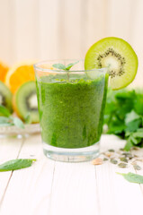 Healthy green smoothie with spinach, kiwi and orange in a glass on light wooden table