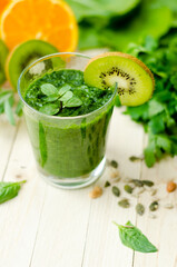 Healthy green smoothie with spinach, kiwi and orange in a glass on light wooden table