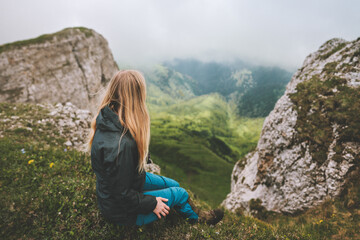 Naklejka na ściany i meble Woman traveling solo sitting on cliff edge enjoying foggy view hiking in mountains outdoor adventure healthy lifestyle vacations