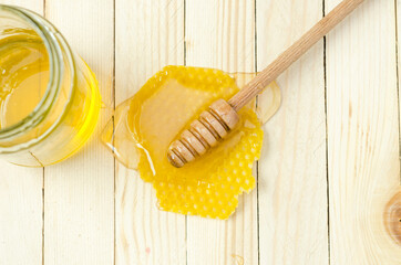 Honey dipper in honey with honeycomb and jar on light wooden table. Top View