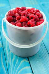 Raspberry bucket on colourful turquoise blue painted wooden boards