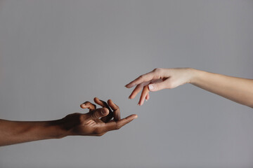Male and female hands reaching out to each other isolated on grey background.