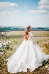 Fototapeta na wymiar A girl in a white wedding dress stands against the backdrop of a beautiful landscape