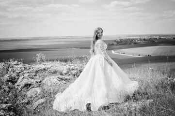 A girl in a white wedding dress stands against the backdrop of a beautiful landscape