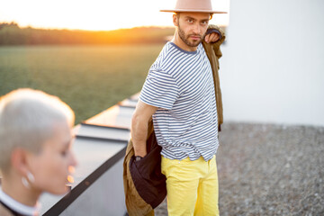 Fototapeta premium Stylish carefree man wearing coat, hanging out on the rooftop with friends at sunset