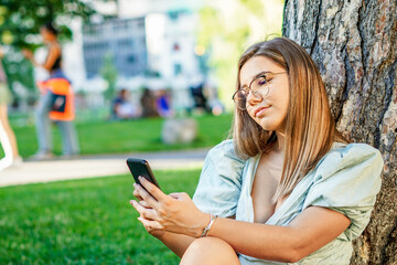 Young girl taking a selfie - Teenager holding smartphone in park - Beautiful adolescent using technology in nature - Summer vibe