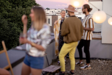 Young stylish friends hang out together talk and having fun on a rooftop party at dusk