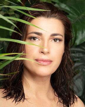 Beautiful natural young woman with flawless fresh clean skin and healthy hair amongst green tropical leaves. Wellness, health and natural body care or spa treatments. Vertical beauty portrait