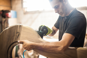 Craftsman is using an electric sander, to smoothen the wood texture. Carpentry concept with wood