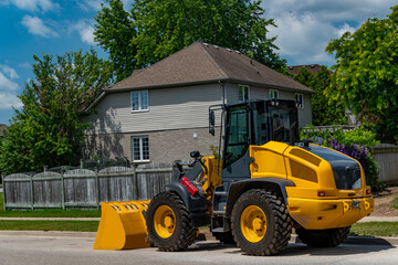 Fototapeta na wymiar Yellow excavator on the road near the house