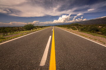 
Empty asphalt road in the middle of nowhere with a symetric view and yellow and white lines and a sunny sky. Catamarca, Argentina