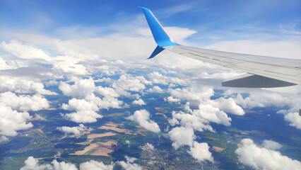 View from the plane window with the wing of a passenger plane on the background of the horizon and the blue sky with beautiful white lush clouds