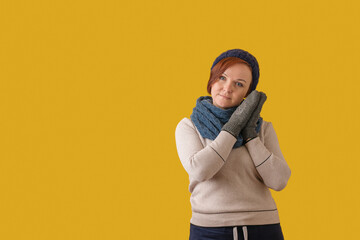 woman in mittens, hat, scarf folded her hands at her face on a yellow background