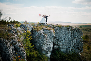 Fototapeta premium Newlyweds stand against the background of rocks and hold colorful smoke in their hands