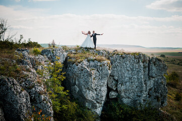 Newlyweds stand against the background of rocks and hold colorful smoke in their hands