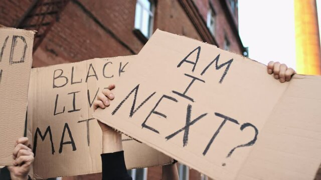 Protesters on the street hold posters above their heads with inscriptions - I STAND WITH YOU, BLACK LIVES MATTER, AM I NEXT
