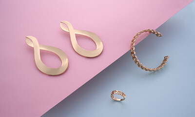 Chain shape bracelet and ring with golden modern earrings pair on pink and blue background