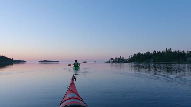 Girl kayaking and then taking break from paddling, mirror like calm water at midnight in Northern Sweden during light Summer night Sun in polar regions. Umea, Sweden.